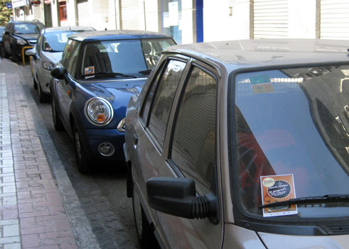 Vehículos aparcados en una calle  de Granada con voletas del Festival 